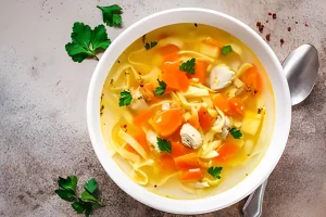 Gluten-free chicken noodle soup in a white bowl with parsley garnish.