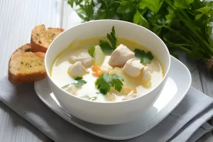 A bowl of steaming chicken soup with vegetables